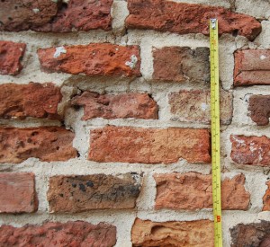 Small, roughly-made, old red bricks, with thick, grey, mortar between. A steel tape shows the thickness to be approximately 5 cm / 2 inches.