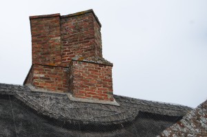 Two adjoining red-brick chimneys, on the apex of a thatched roof.